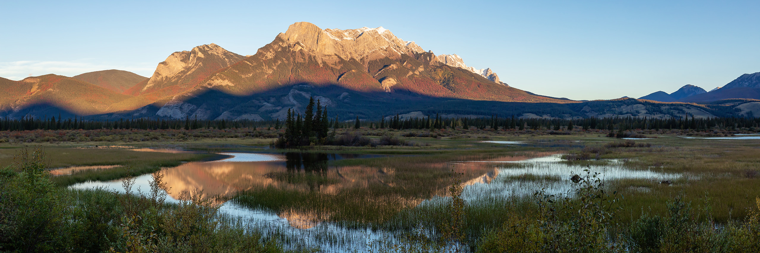 Panoramic landscape of the Canadian Rocky Mountains during a sunny sunrise.